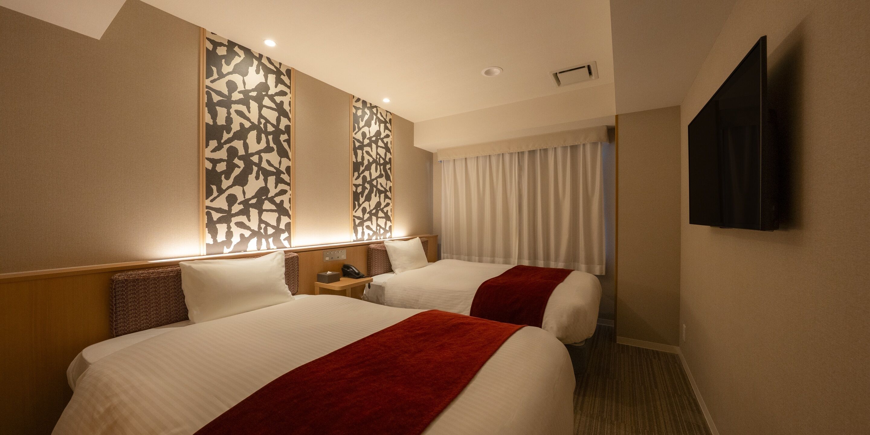 Une chambre d’hôtel avec deux lits, un téléviseur fixé au mur et une fenêtre avec des rideaux.