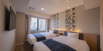 A hotel room with two beds, a flat-screen TV, a window with blinds, and a city view.