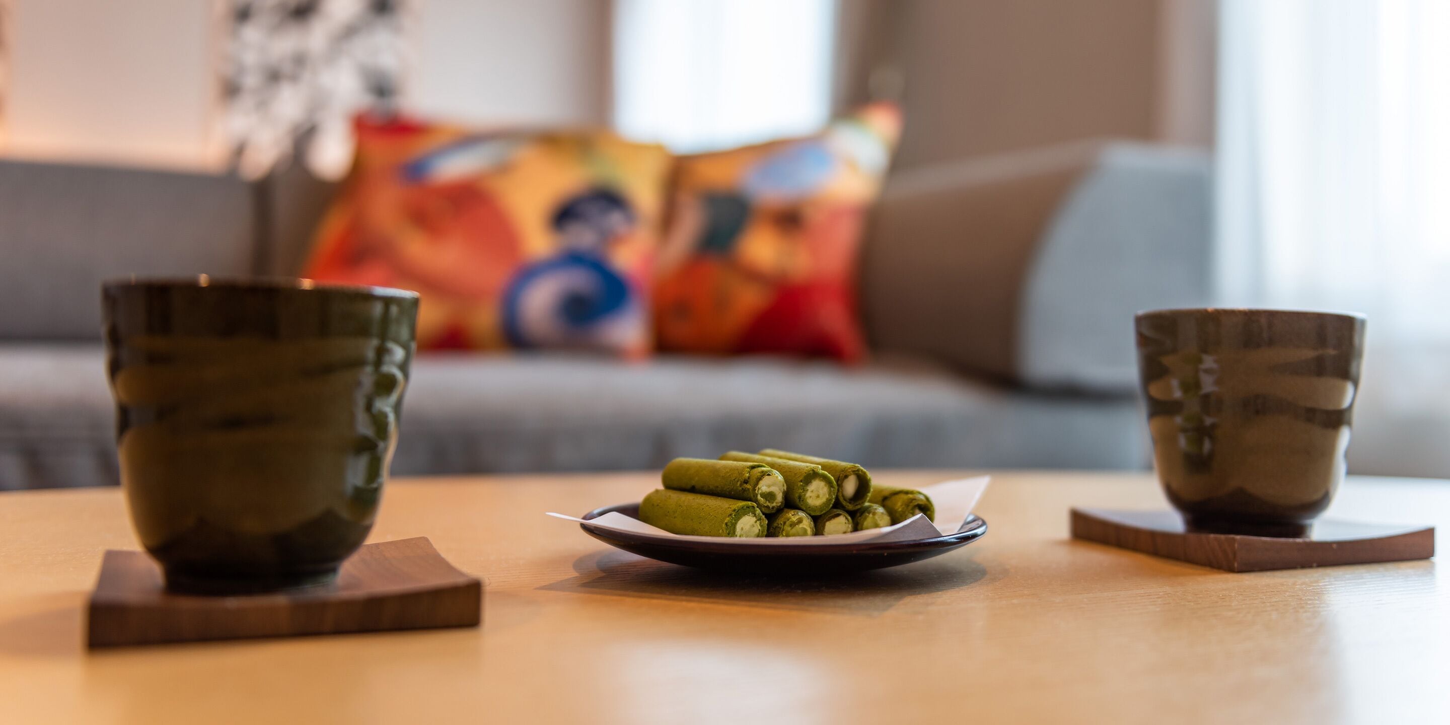 A table with two ceramic cups and a plate of green tea rolls.