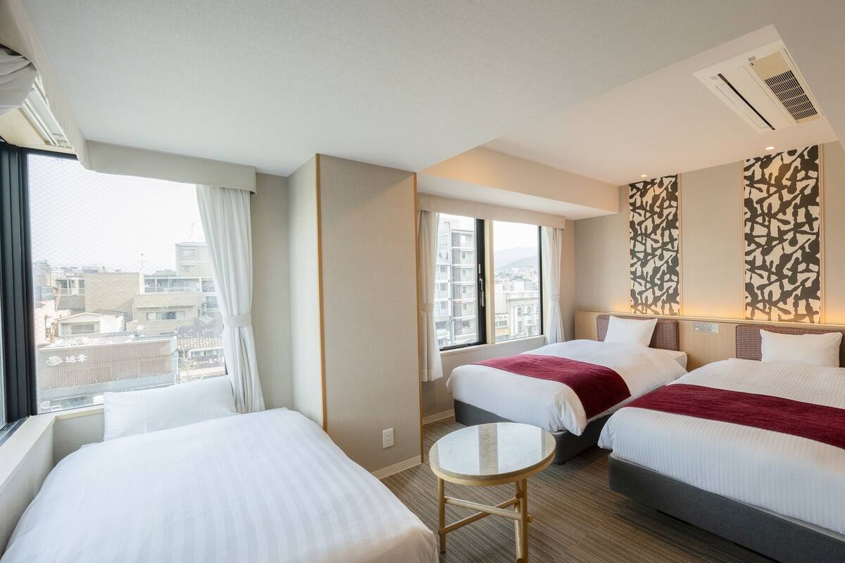 Une chambre d’hôtel avec deux lits, une petite table et une vue sur la ville grâce à de grandes fenêtres.