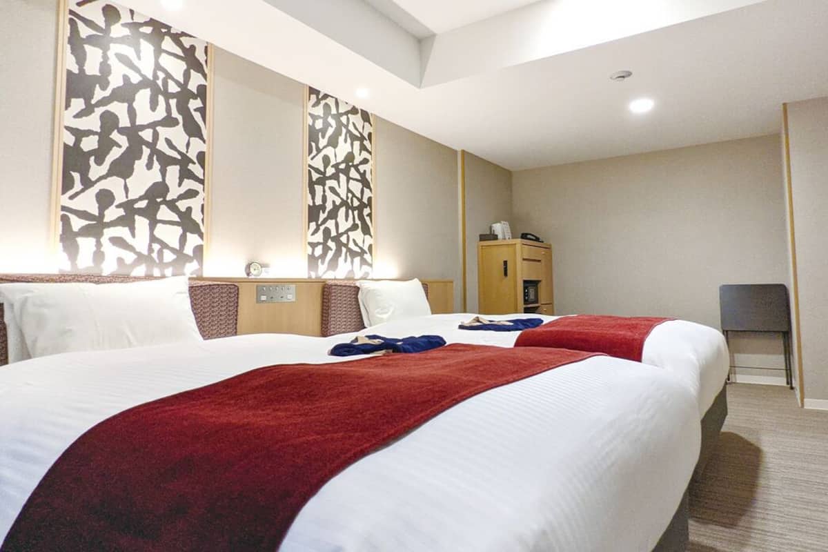 Une chambre d’hôtel avec deux lits, un bureau, une chaise, une armoire et un miroir.