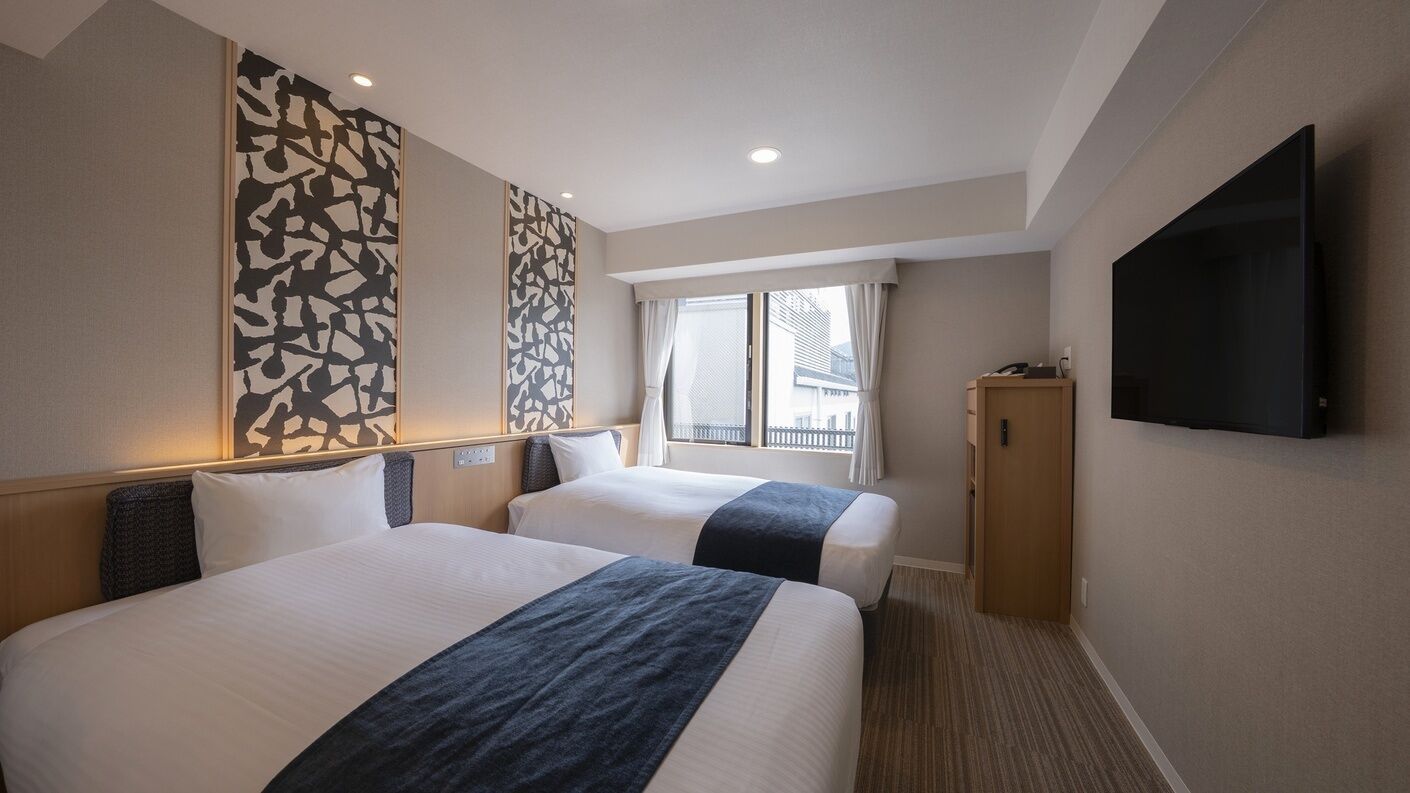Une chambre d’hôtel avec deux lits, un téléviseur à écran plat, une fenêtre avec des rideaux et une œuvre d’art accrochée au mur.