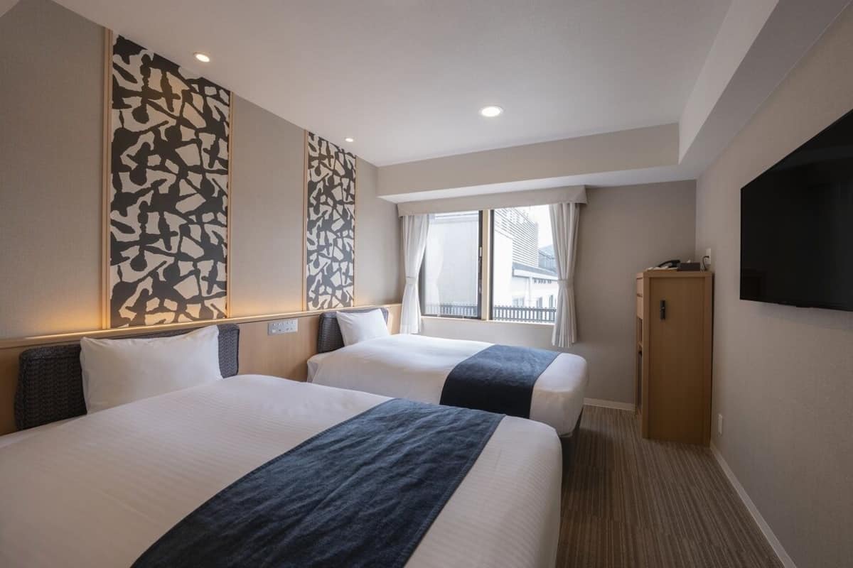 Une chambre d’hôtel avec deux lits, un téléviseur à écran plat, une fenêtre avec des rideaux et une œuvre d’art accrochée au mur.