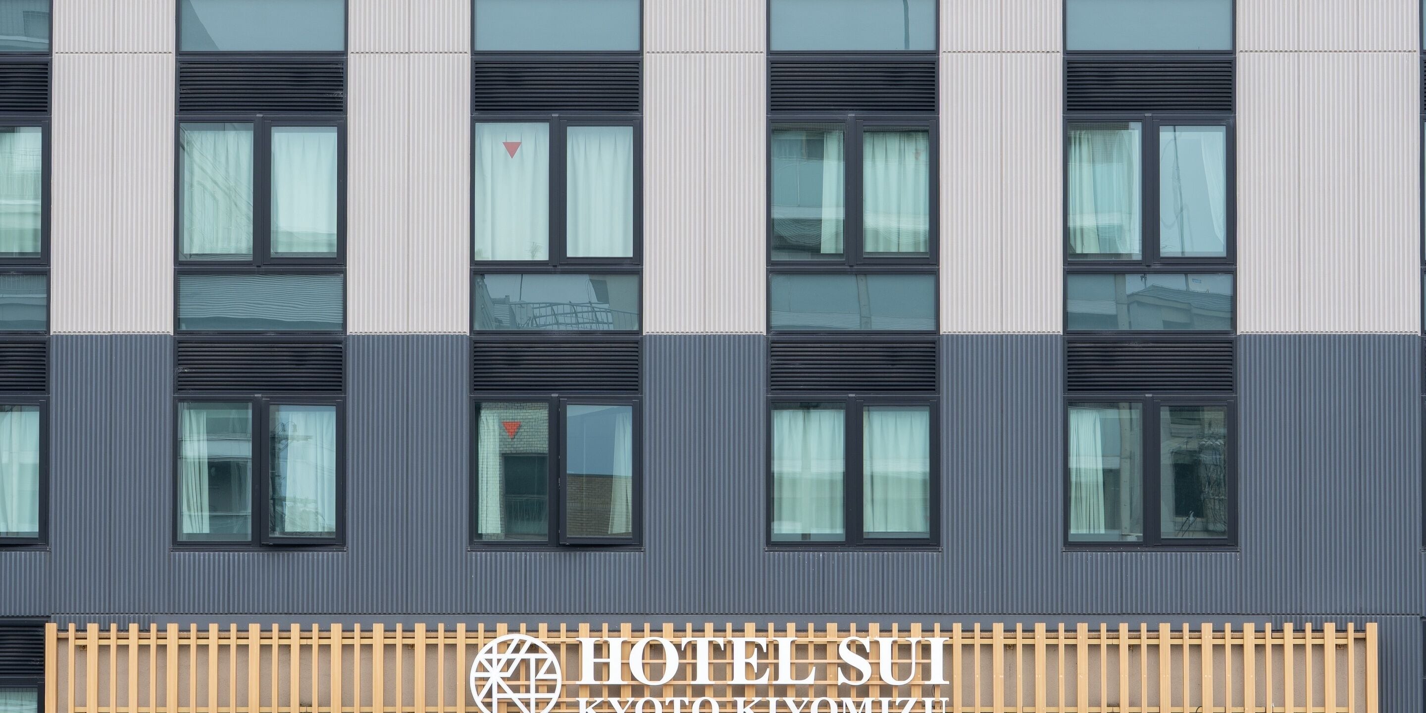 La façade d’un hôtel, ornée de nombreuses fenêtres, une enseigne indiquant « HÔTEL SUI KYOTO KIMIZU » et une clôture en bois.