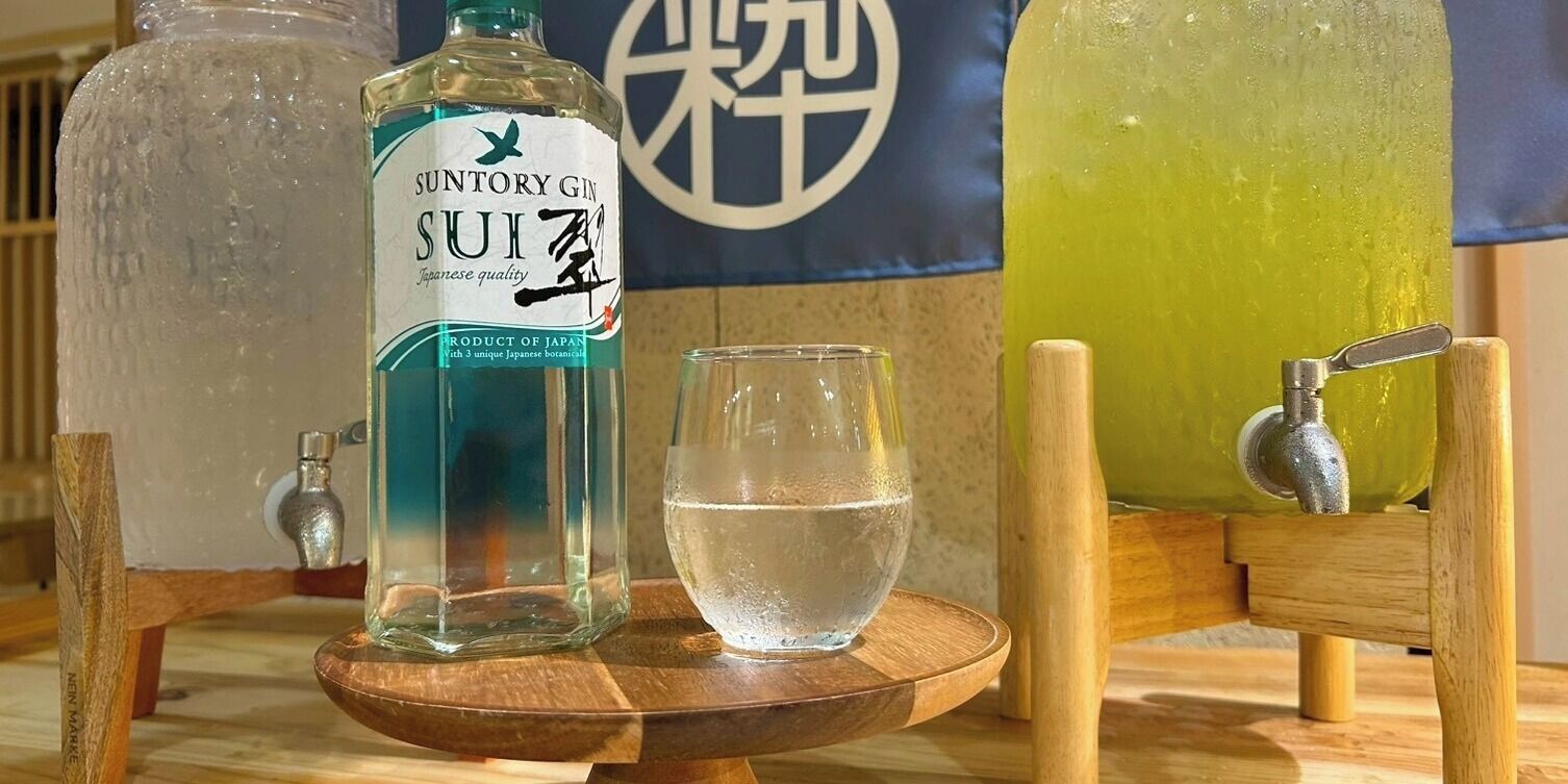 Eine Suntory-Gin-Flasche, ein Glas Wasser und eine Holztresen mit Zapfhahn.