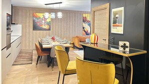 Un comedor moderno con una mesa de madera dispuesta para cuatro personas, rodeada de sillas amarillas. Hay pinturas abstractas en las paredes y una foto enmarcada de una copa de vino etiquetada como "PERCEPTION".