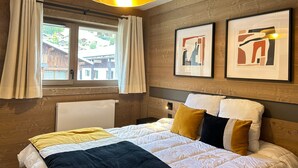 Un dormitorio con cama, ventana con cortinas, pared de madera y dos cuadros enmarcados.