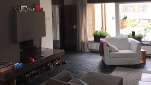 A modern living room with a sofa, a coffee table, and a fireplace. There is a balcony with a railing and a view of the outside. - Grote Familiewoning Heel Dicht bij het Strand (Noordwijk Zh)