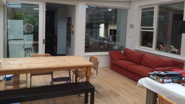 A sunlit room with a wooden table, a red sofa, and a window with toys. - Grote Familiewoning Heel Dicht bij het Strand (Noordwijk Zh)