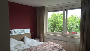A bedroom with a bed, a nightstand, a window with curtains, and a radiator. - Grote Familiewoning Heel Dicht bij het Strand (Noordwijk Zh)