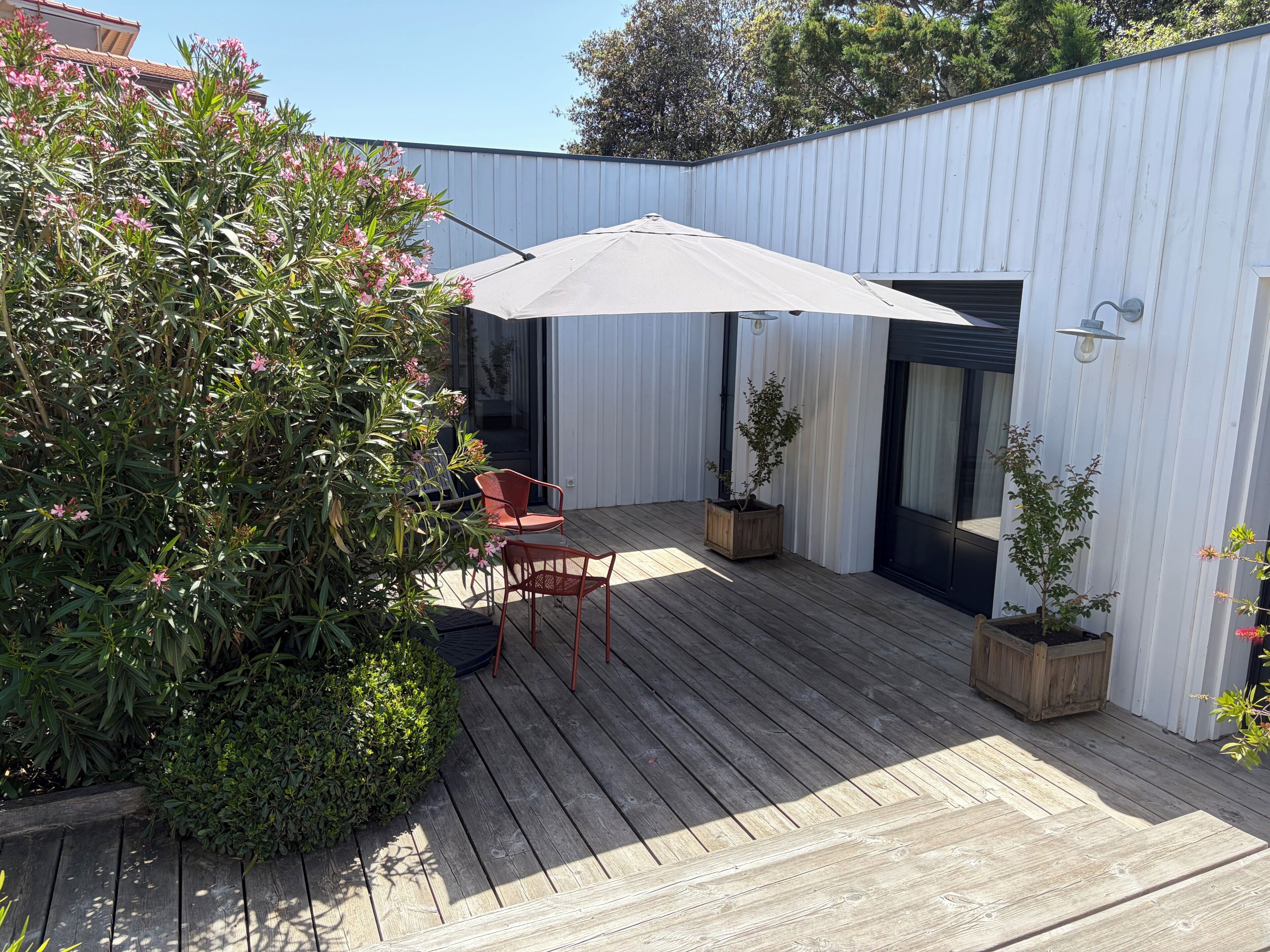 Une terrasse en bois avec deux chaises, un grand parasol et des plantes en pot.