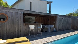 A wooden deck with a pool, outdoor seating, and a covered area with a grill.
