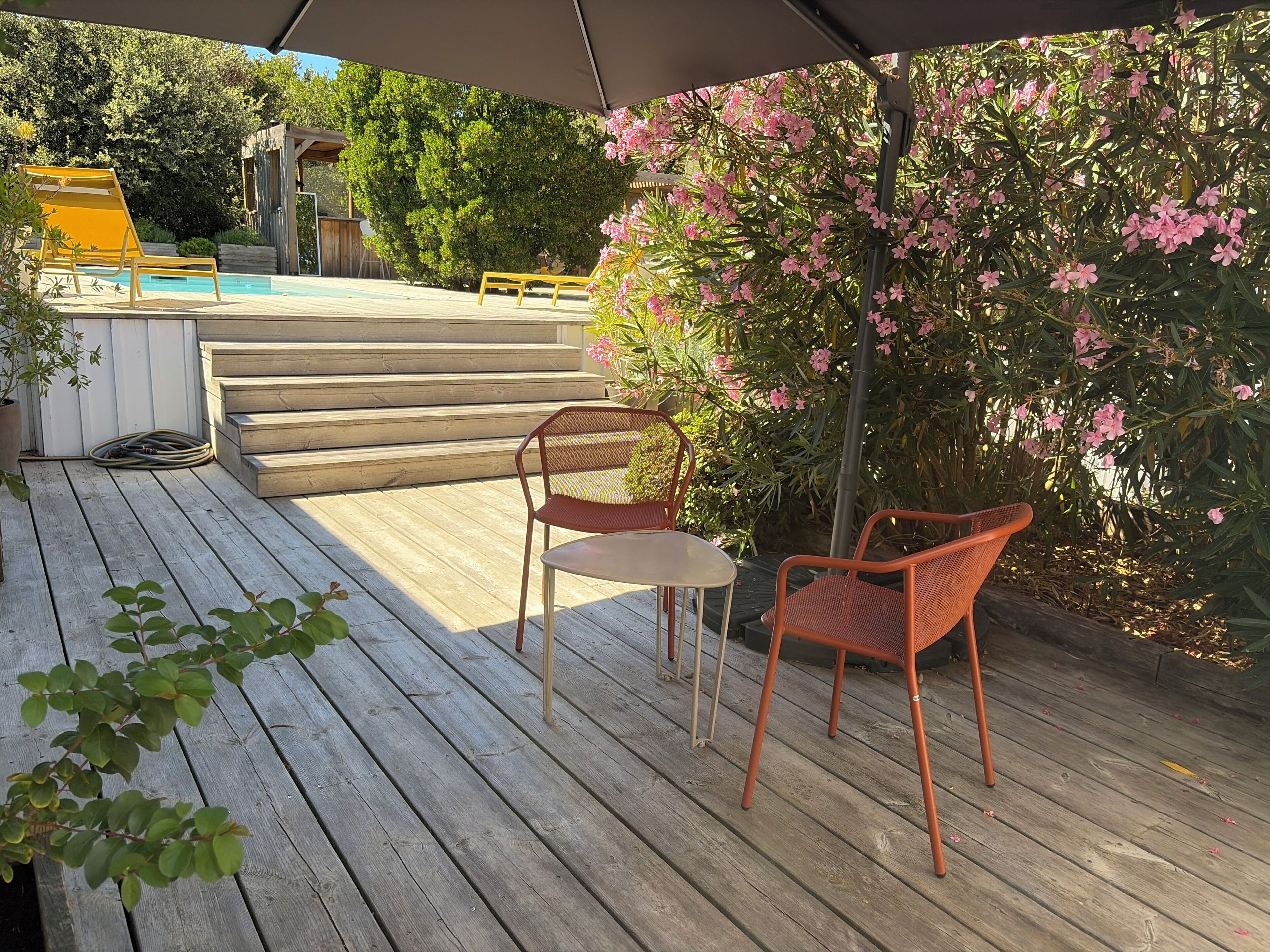 Une terrasse en bois avec des meubles d’extérieur, une piscine et un escalier menant à un espace abrité.