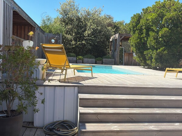 A wooden deck with a pool, outdoor chairs, and a potted plant.