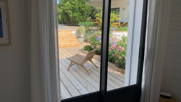 A view through a sliding glass door to a wooden deck with outdoor furniture and potted plants.