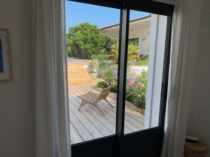 A view through a sliding glass door to a wooden deck with outdoor furniture and potted plants.