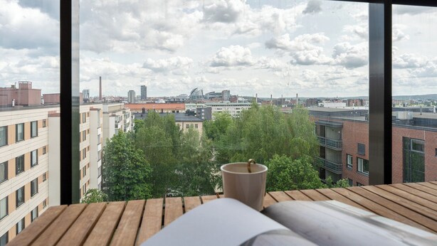 Ein Schlafzimmer mit großem Fenster und Blick auf die Stadtlandschaft, einem hölzernen Kopfteil und einer Tasse auf dem Fensterbrett.
