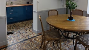 A dining area with a round wooden table, four chairs, a potted plant, and a kitchen in the background. - Maison de Vacance Tout Confort Avec Piscine (saint benoit du sault)