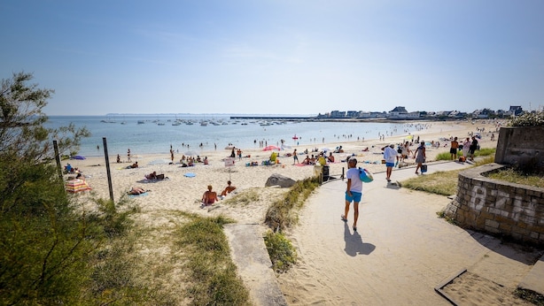 Een strand met heldere lucht, zandstrand en mensen die van de zon genieten.