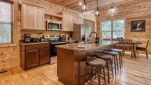 A wooden cabin interior with a kitchen featuring a central island, bar stools, and a dining area with a table and chairs. - Splish-N-Splash · Private Indoor Pool, Hot Tub, $560 FREE tickets each paid day (Sevierville)