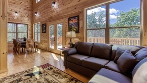 A spacious room with wooden walls, large windows, a dining area, and a sofa. - Splish-N-Splash · Private Indoor Pool, Hot Tub, $560 FREE tickets each paid day (Sevierville)