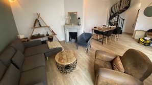 A living room with a sofa, armchair, round coffee table, fireplace, dining table with chairs, and a spiral staircase.