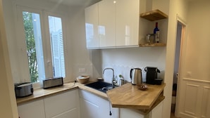 A modern kitchen with white cabinets, a wooden countertop, a sink, and a coffee maker.