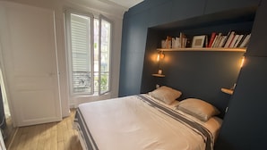 A bedroom with a bed, a bookshelf, and a window with blinds.