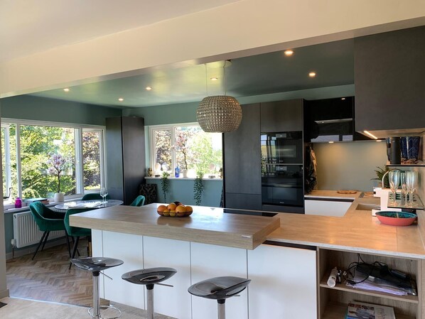 A modern kitchen with a central island, bar stools, and a hanging light fixture.