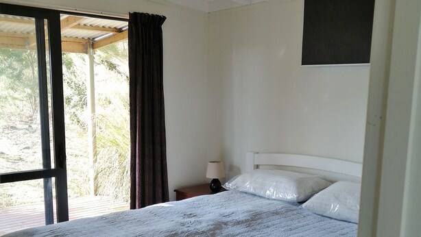 A bedroom with a bed, a nightstand, a window with curtains, and a wall-mounted TV.