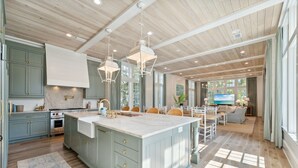 Een ruime keuken met een groot eiland, houten plafond en veel natuurlijk licht.