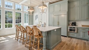 Een ruime keuken met een groot kookeiland, houten plafond en lichtblauwe keukenkastjes.