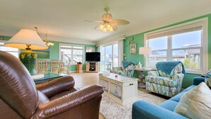 Een woonkamer met een bruine leren bank, een blauwe fauteuil en een televisie op een houten dressoir.