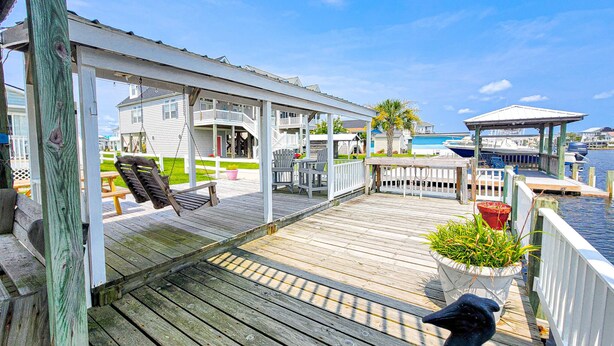 Een houten terras met buitenmeubilair, een overdekt gedeelte en uitzicht op de jachthaven.