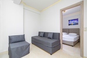 Un dormitorio moderno con un sofá gris, una silla pequeña y una cama con ropa de cama blanca.