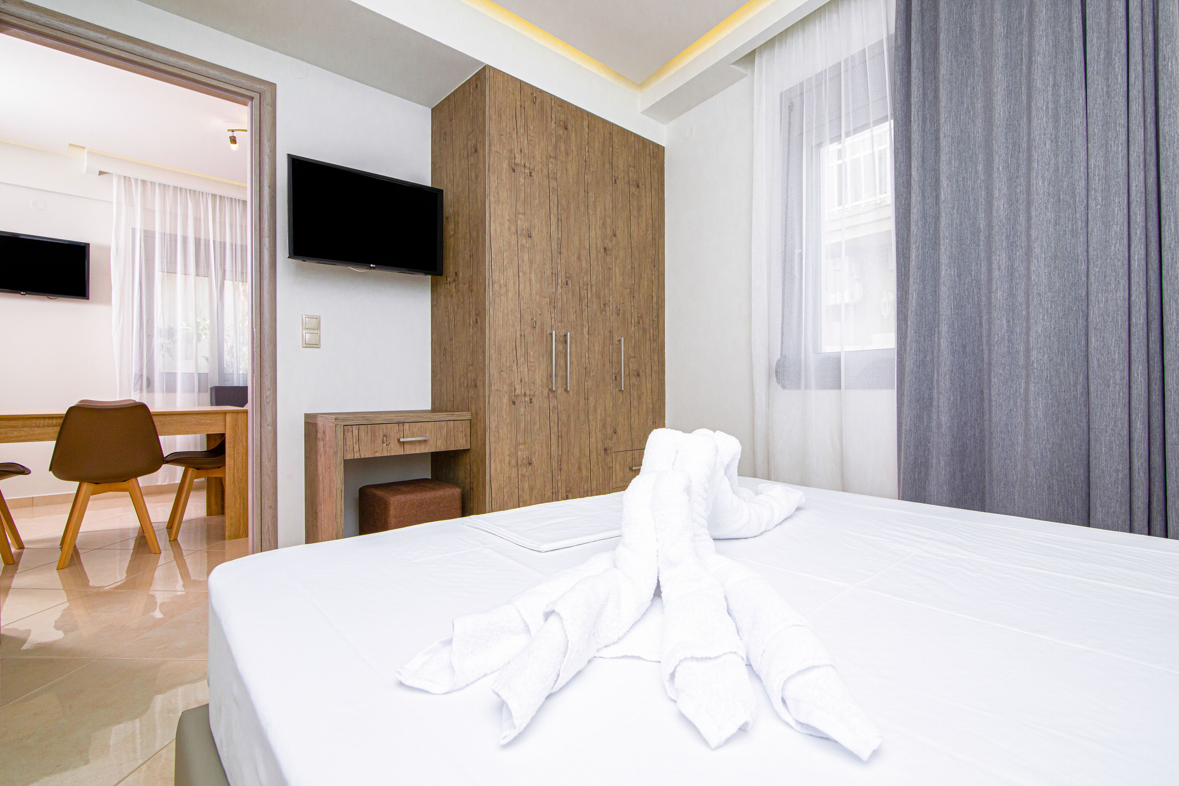 A hotel room with a bed, a wooden wardrobe, a desk with a chair, and a television on the wall.