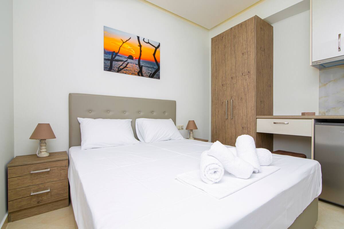 Ein Hotelzimmer mit einem Bett, einem Holzschrank, einem Nachttisch mit Lampen und einem Sonnenuntergangsbild.
