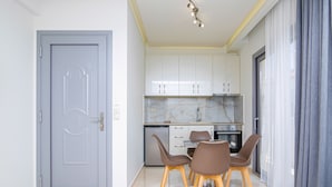 A modern kitchen with white cabinets, a marble countertop, and a dining area with brown chairs. - Amara Suites and Studios (Hersonissos)