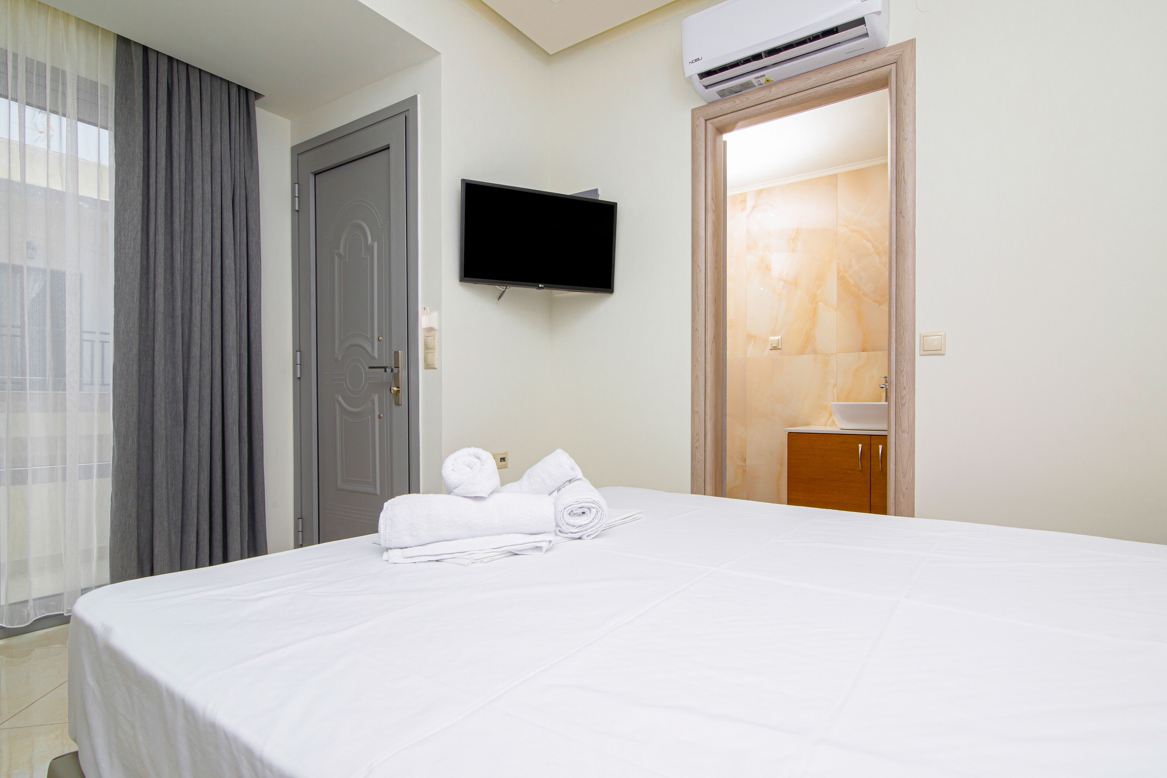A hotel room with a bed, a television mounted on the wall, and a bathroom visible through an open door.