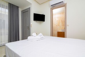A hotel room with a bed, a television mounted on the wall, and a bathroom visible through an open door. - Amara Suites and Studios (Hersonissos)