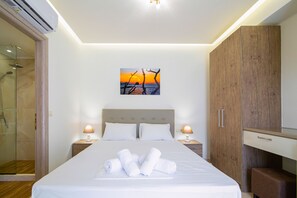 Una cama bien hecha con toallas enrolladas, un armario de madera, una mesita de noche con lámpara y un box de ducha de cristal.