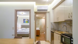 A compact kitchen with modern appliances, a dining area with a wooden table, and a visible bathroom with a shower. - Amara Suites and Studios (Hersonissos)
