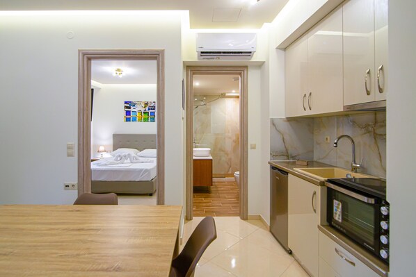 A compact kitchen with modern appliances, a dining area with a wooden table, and a visible bathroom with a shower. - Amara Suites and Studios (Hersonissos)