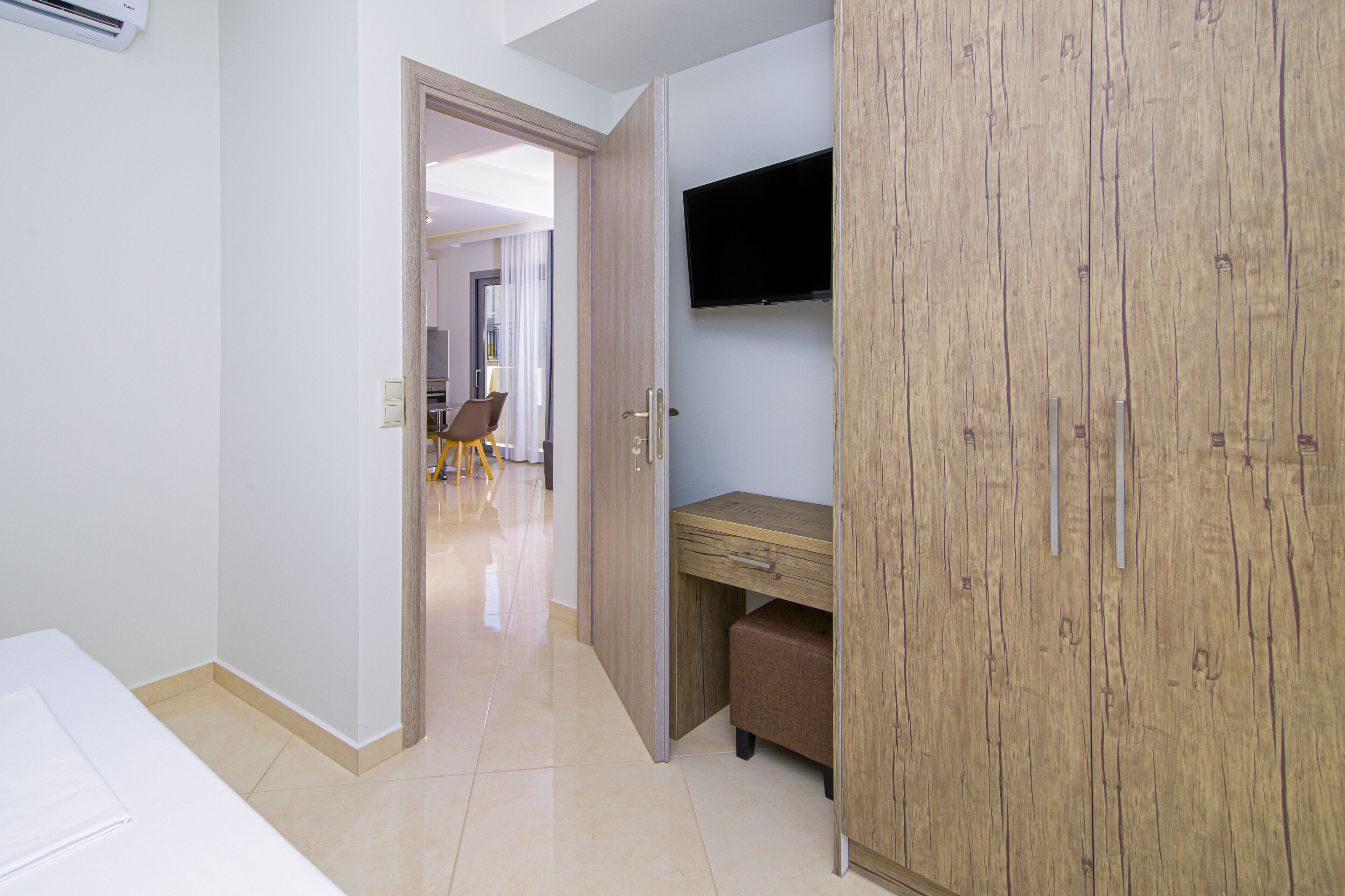 A hotel room with a wooden wardrobe, a desk, and a TV mounted on the wall.