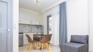 A modern living room with a grey sofa, a dining area with brown chairs, and a kitchen with white cabinets. - Amara Suites and Studios (Hersonissos)