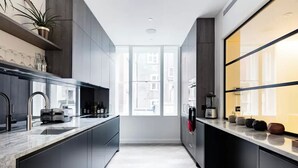 Una cocina moderna con armarios oscuros, encimera de mármol y vistas a la ciudad a través de amplios ventanales.