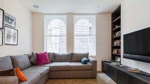 Una sala de estar con un sofá modular, un televisor de pantalla plana y una estantería.