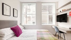 Un dormitorio moderno con una cama, un escritorio y un televisor.
