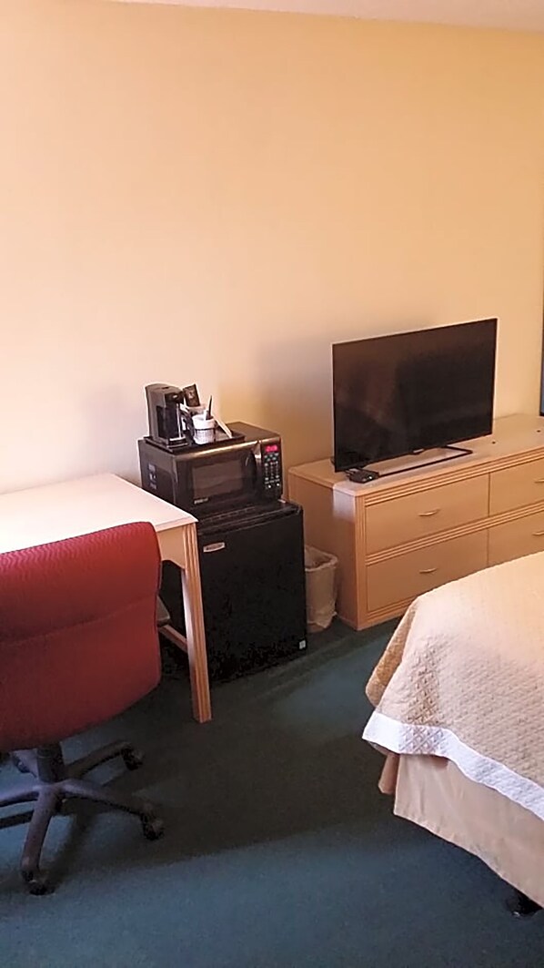 Una habitación de hotel con escritorio, microondas, televisor, una silla de oficina roja y una cama.