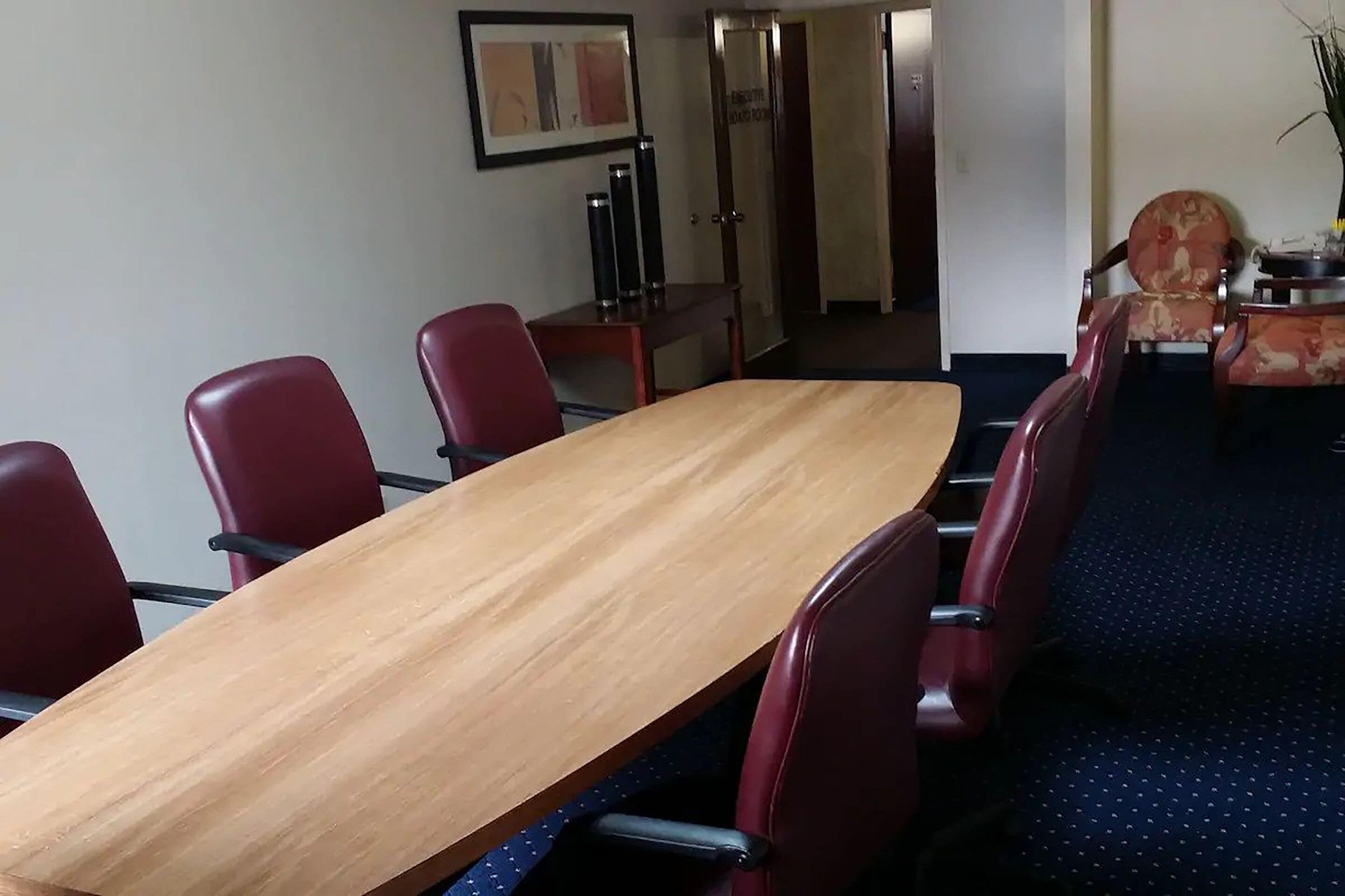 A conference room with a long wooden table and red chairs.